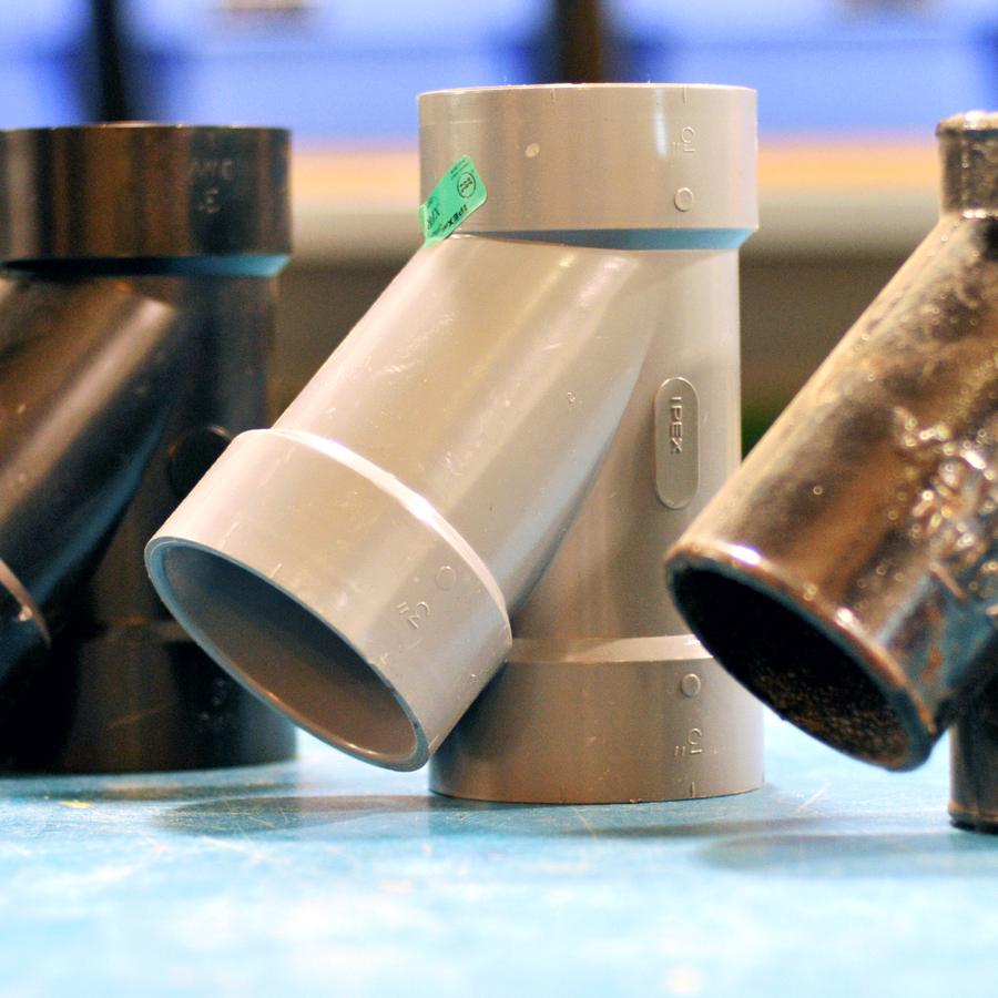 Three drain pipe fittings: black ABS, grey PVC and cast iron
