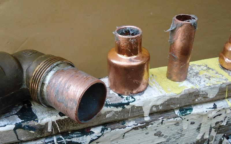 Copper and brass pipe fittings lined up on a paint-spattered board